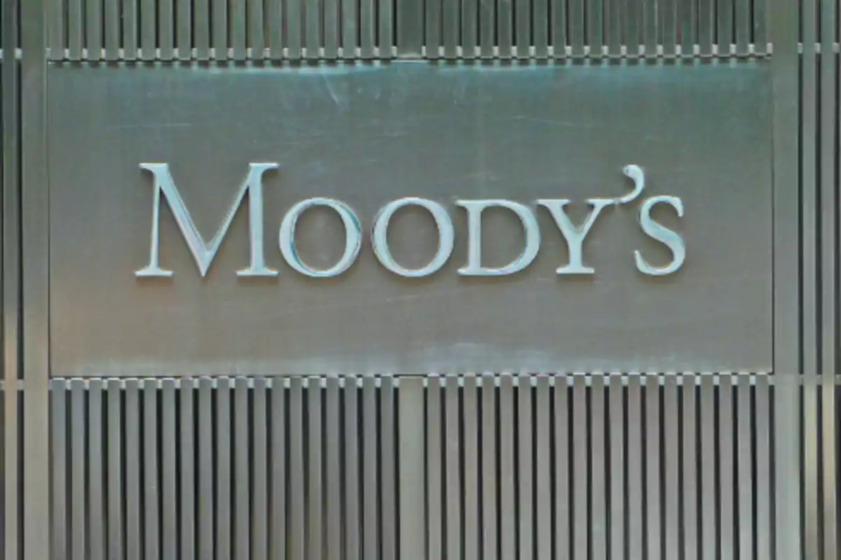 Un letrero metálico con el nombre "Moody's" en letras grandes y plateadas sobre un fondo con líneas verticales.