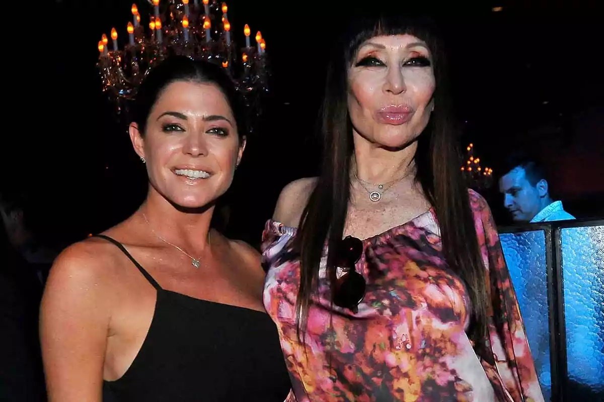 Dos mujeres posan juntas en un evento elegante con un candelabro iluminado al fondo. Dos mujeres posan juntas en un evento elegante con un candelabro iluminado al fondo.