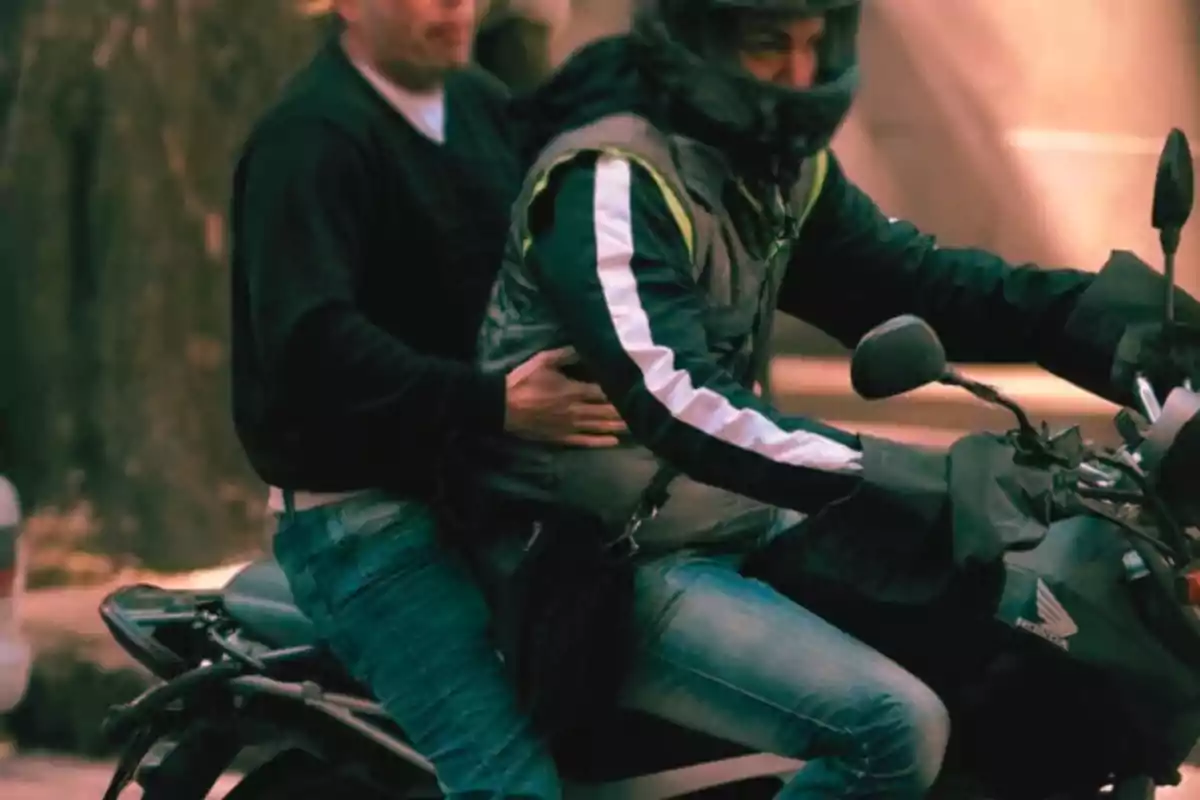Two people are riding a motorcycle, the driver is wearing a helmet and the passenger is holding onto their waist. Two people are riding a motorcycle, the driver is wearing a helmet and the passenger is holding onto their waist.