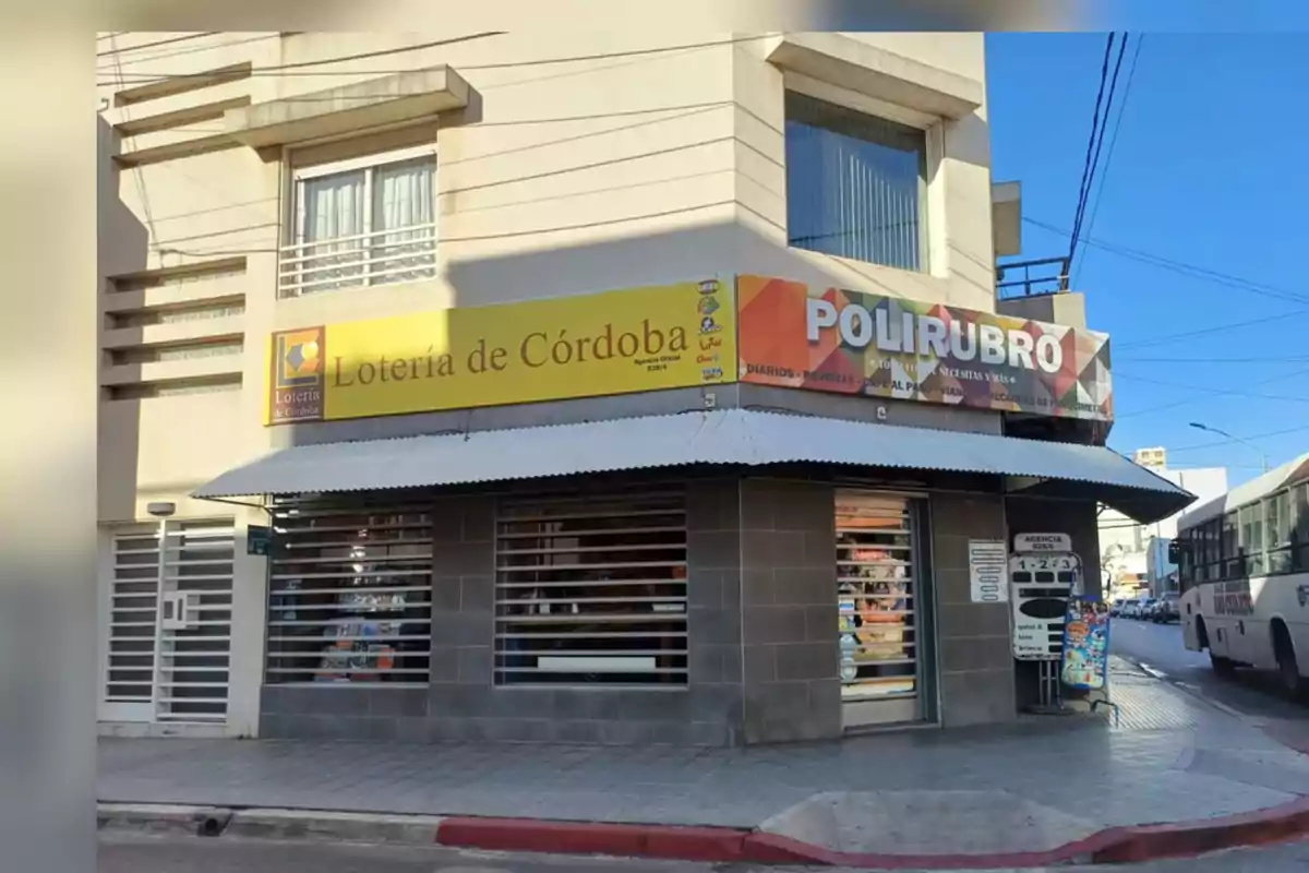 Corner of a building housing a lottery agency and a general store, with yellow and colorful signs, large windows, and a bus stopped on the street.