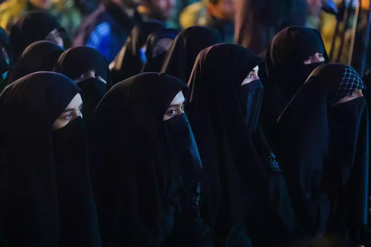 Group of women wearing black veils alertly watching an event in a dark setting Group of women wearing black veils alertly watching an event in a dark setting