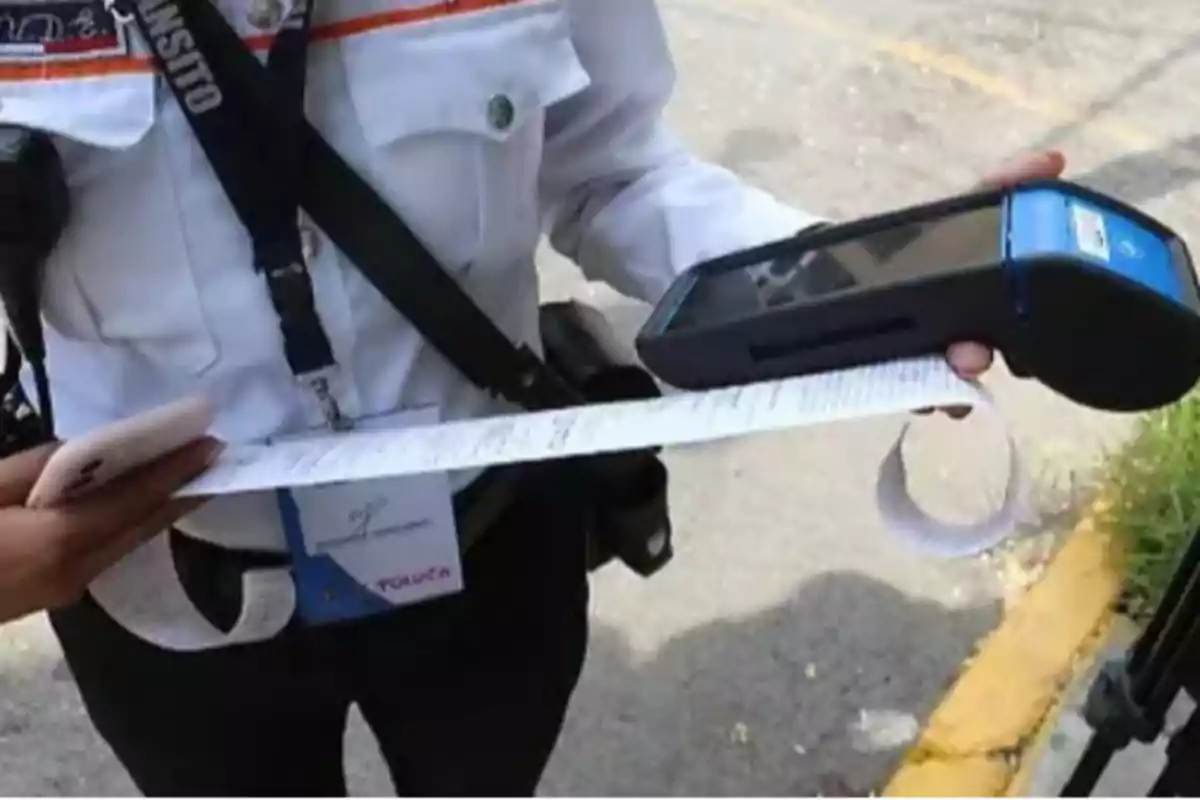 Una persona con uniforme de tránsito sostiene un dispositivo electrónico y un recibo impreso en la calle.