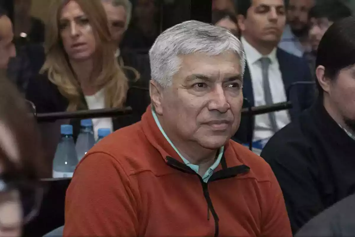 Gray-haired man in an orange sweater sitting among other people in a formal setting Gray-haired man in an orange sweater sitting among other people in a formal setting