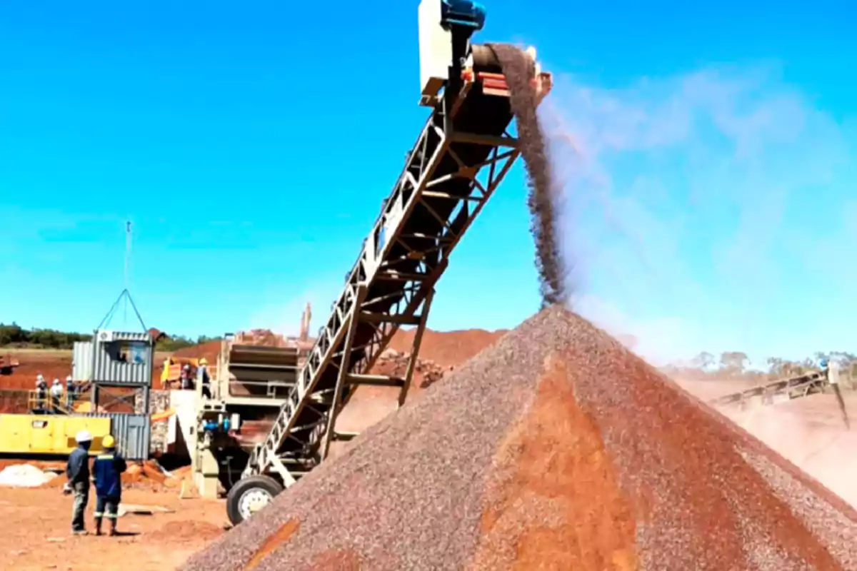 Una cinta transportadora descarga material en un gran montón en un sitio de construcción con trabajadores observando.