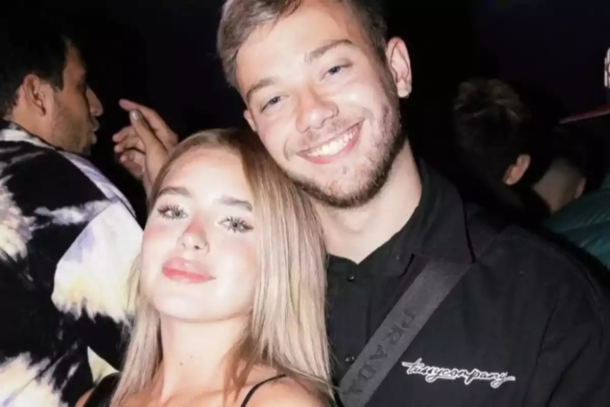 Una pareja joven sonríe mientras posa para una foto en un ambiente de fiesta.