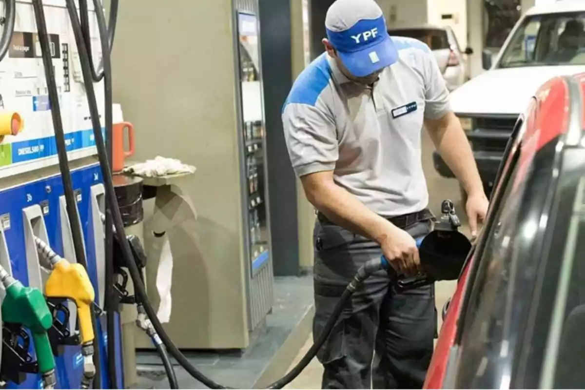 Un empleado de una estación de servicio YPF está llenando el tanque de un automóvil rojo con combustible.