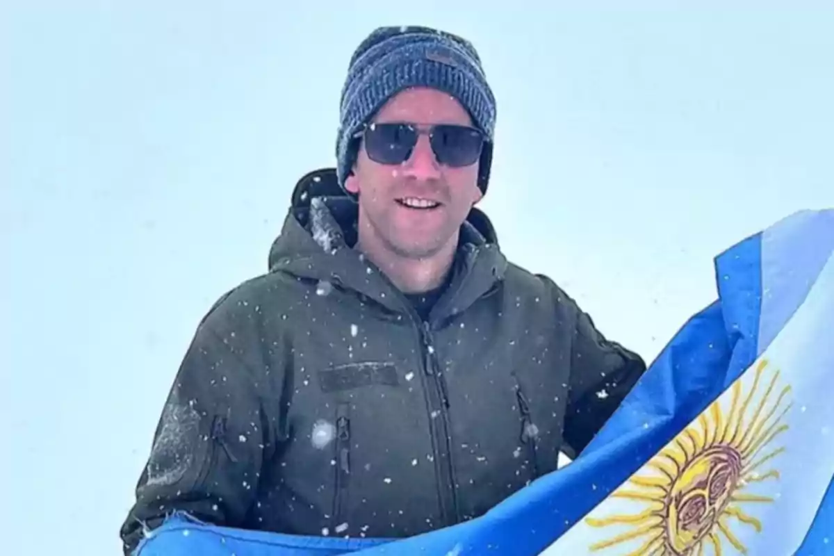 Nahuel Gallo, el gendarme argentino detenido en Venezuela con gafas de sol y gorro sosteniendo una bandera argentina en un entorno nevado.