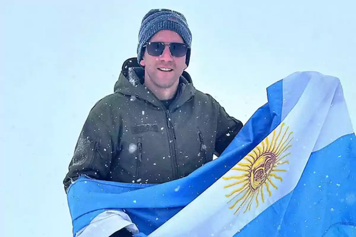 Hombre con gafas de sol y gorro sosteniendo una bandera de Argentina en un entorno nevado Hombre con gafas de sol y gorro sosteniendo una bandera de Argentina en un entorno nevado