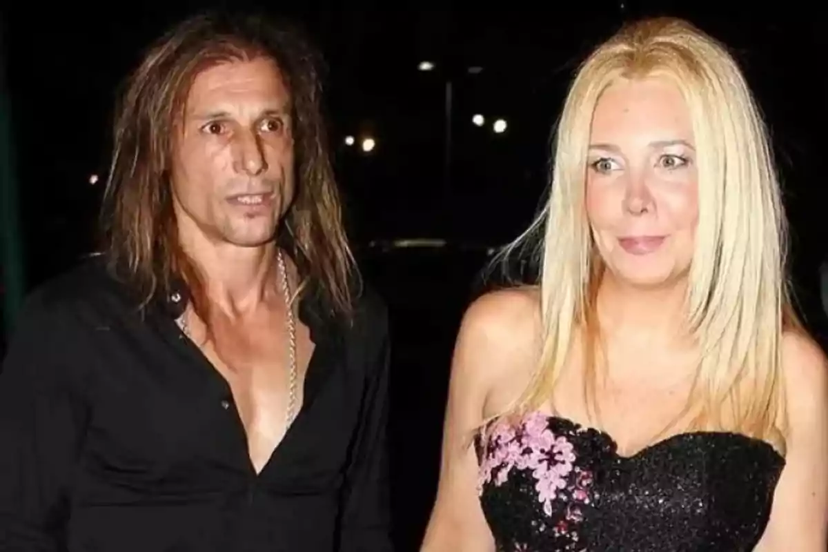 Una pareja posando en un evento nocturno, el hombre lleva una camisa negra y la mujer un vestido negro con detalles florales. Una pareja posando en un evento nocturno, el hombre lleva una camisa negra y la mujer un vestido negro con detalles florales.