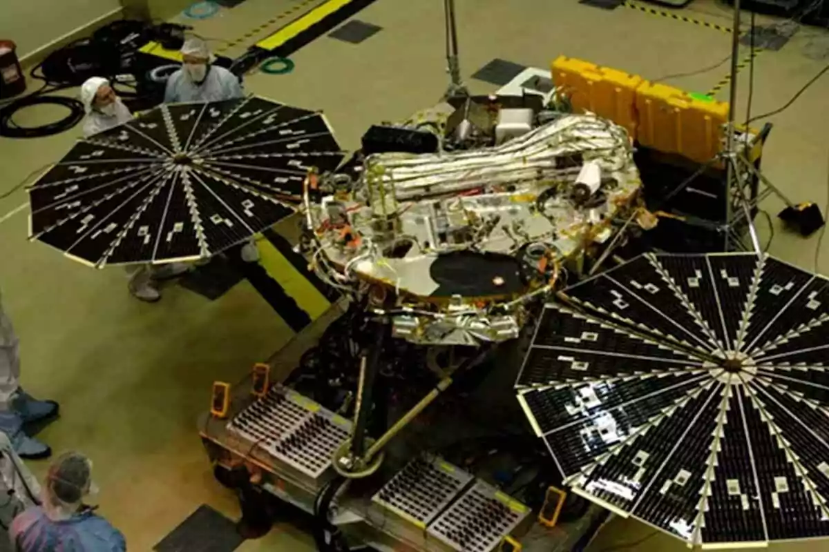 Un equipo de ingenieros trabaja en un laboratorio con un módulo espacial equipado con paneles solares desplegados. Un equipo de ingenieros trabaja en un laboratorio con un módulo espacial equipado con paneles solares desplegados.