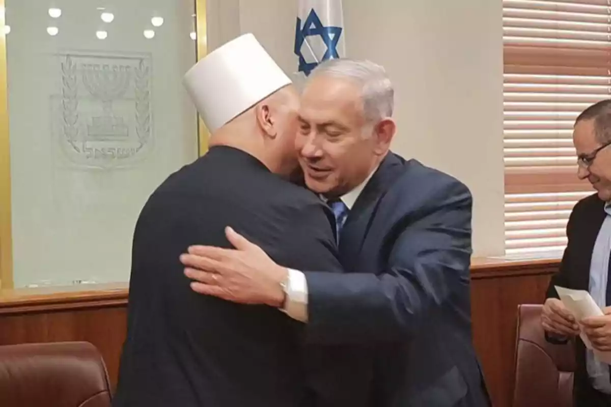 Two people are hugging in a meeting room, one of them is wearing a white hat and the other a dark suit.