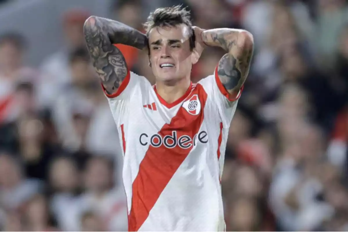 Soccer player with a frustrated expression on the field, wearing the River Plate jersey.