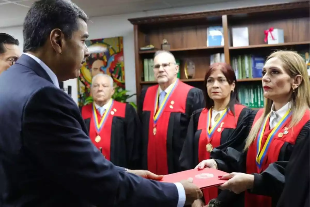 Un grupo de personas con togas y medallas se encuentran en una ceremonia formal, una de ellas entrega un documento a un hombre de traje.