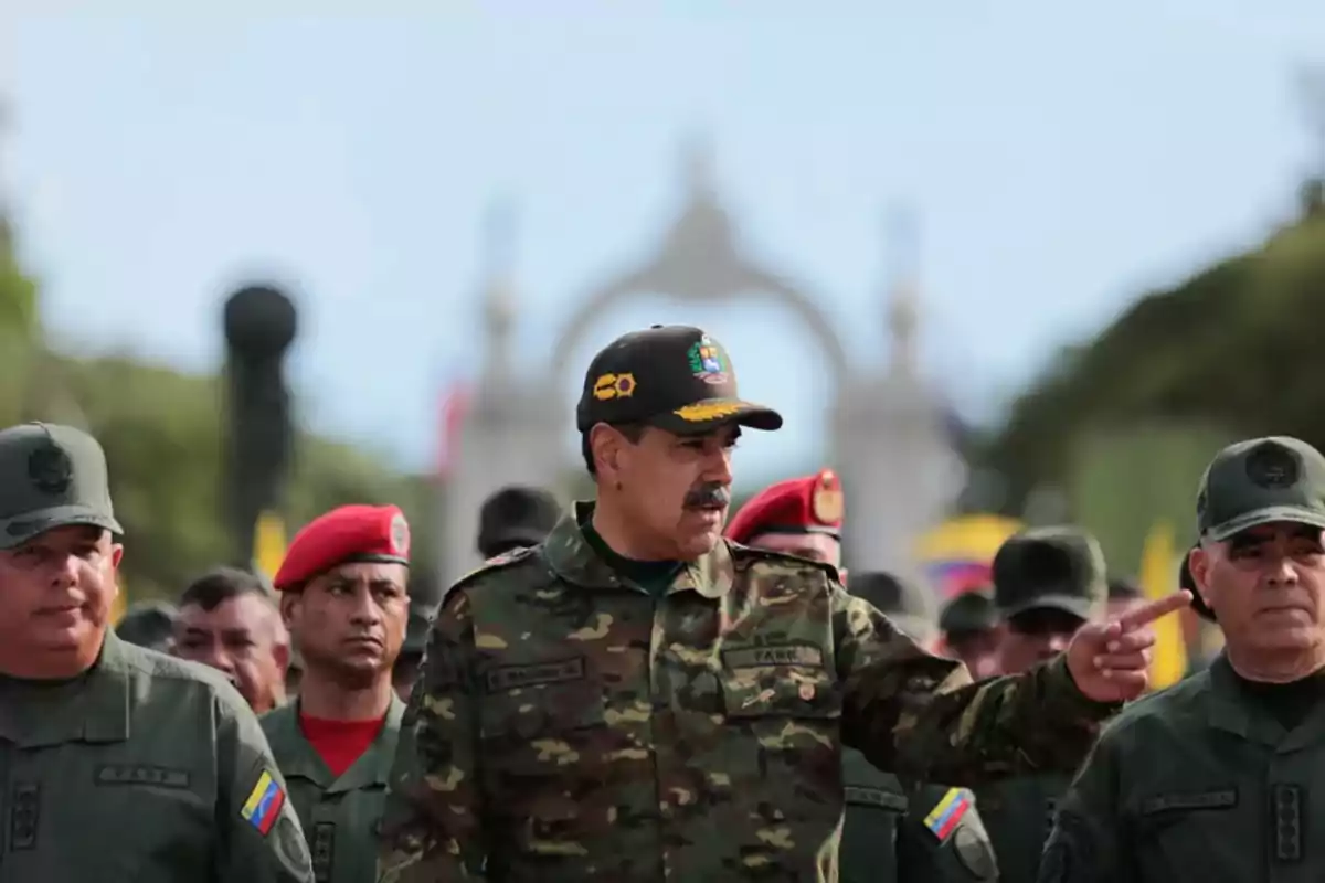 Un grupo de militares en uniforme camuflado y boinas rojas y verdes está reunido al aire libre con un hombre en el centro señalando hacia un lado.