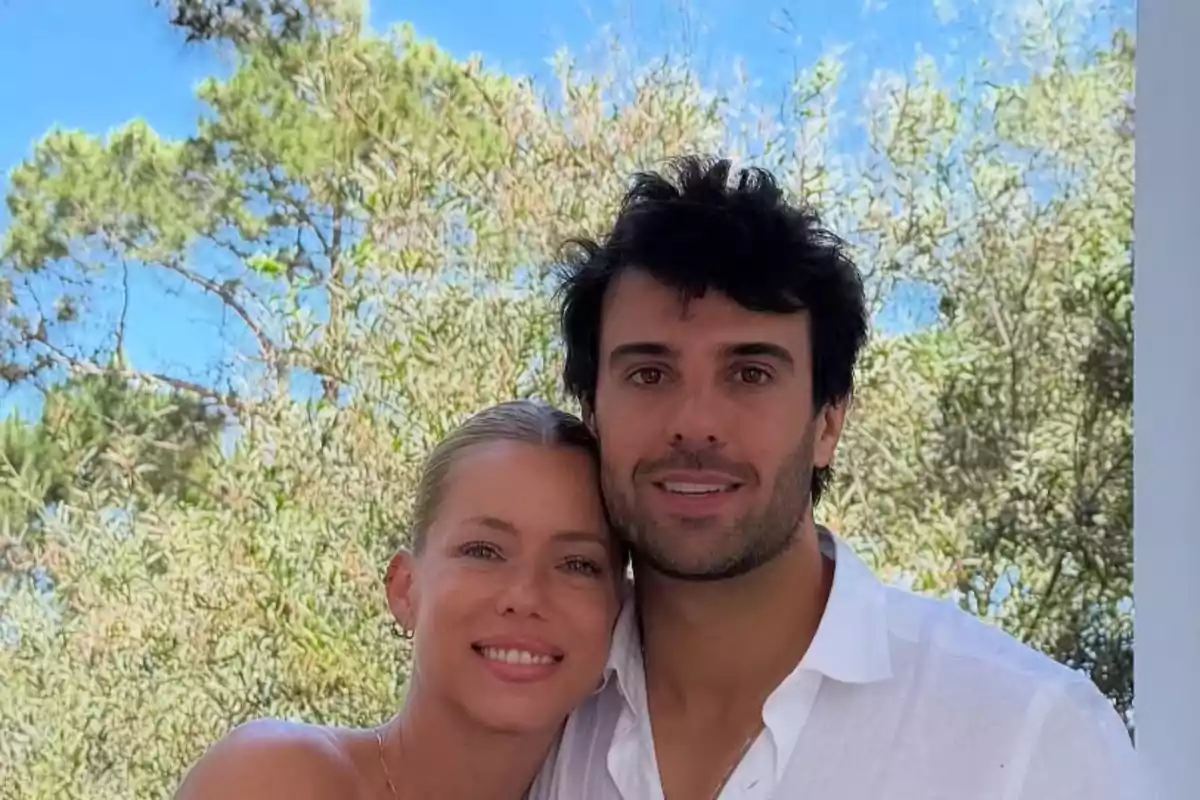 Pareja abrazada sonriendo al aire libre con árboles y cielo azul de fondo