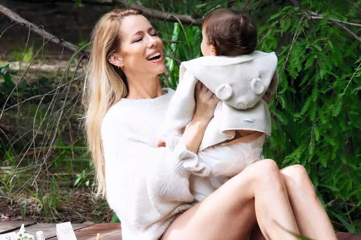 Una mujer sonriente sostiene a un bebé en un entorno natural con vegetación verde. Una mujer sonriente sostiene a un bebé en un entorno natural con vegetación verde.