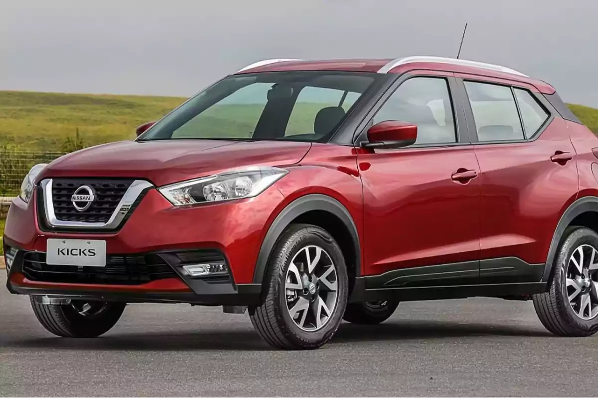 Un SUV Nissan Kicks rojo estacionado en una carretera con un paisaje verde de fondo.