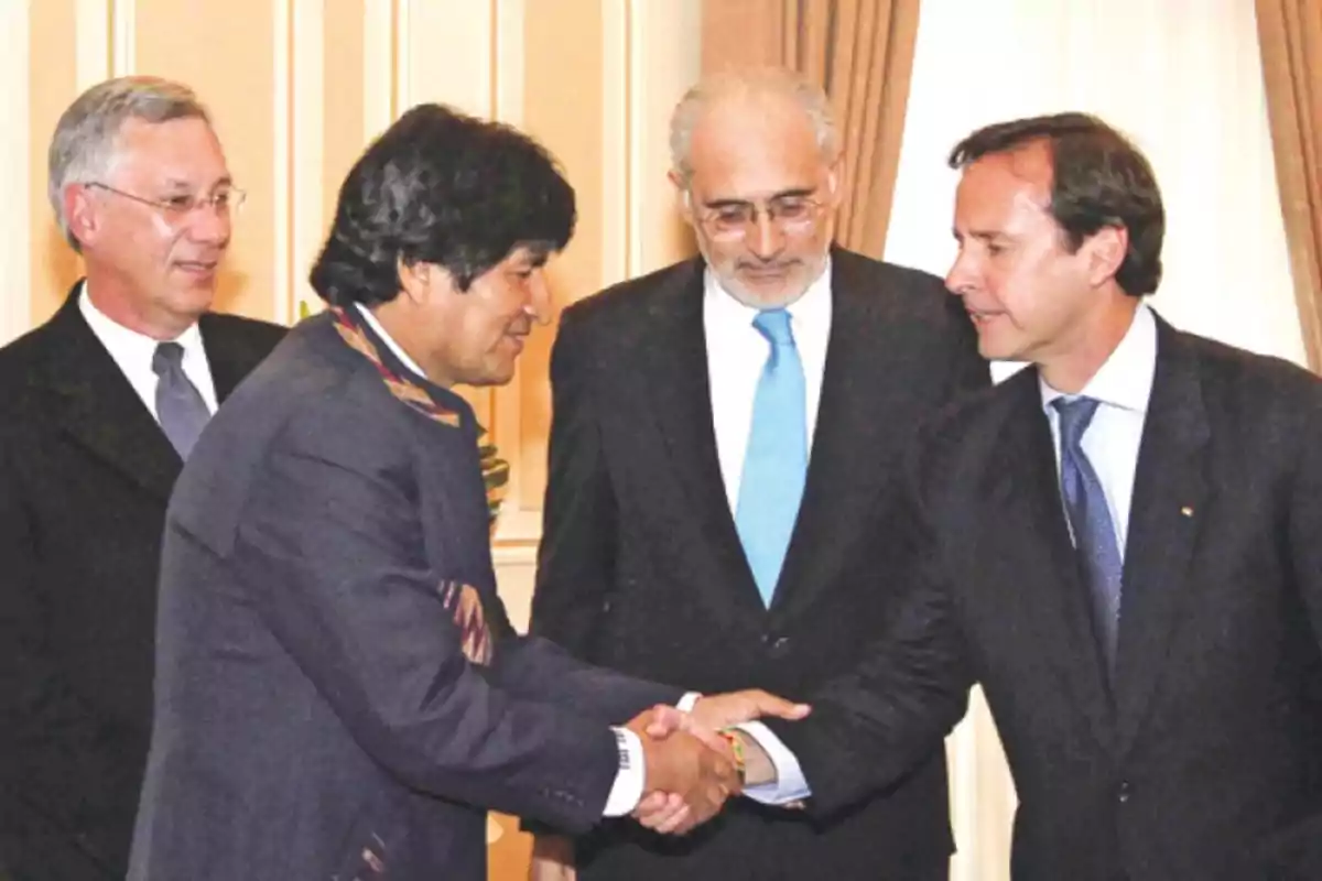 Cuatro hombres vestidos de traje se saludan y conversan en un ambiente formal.