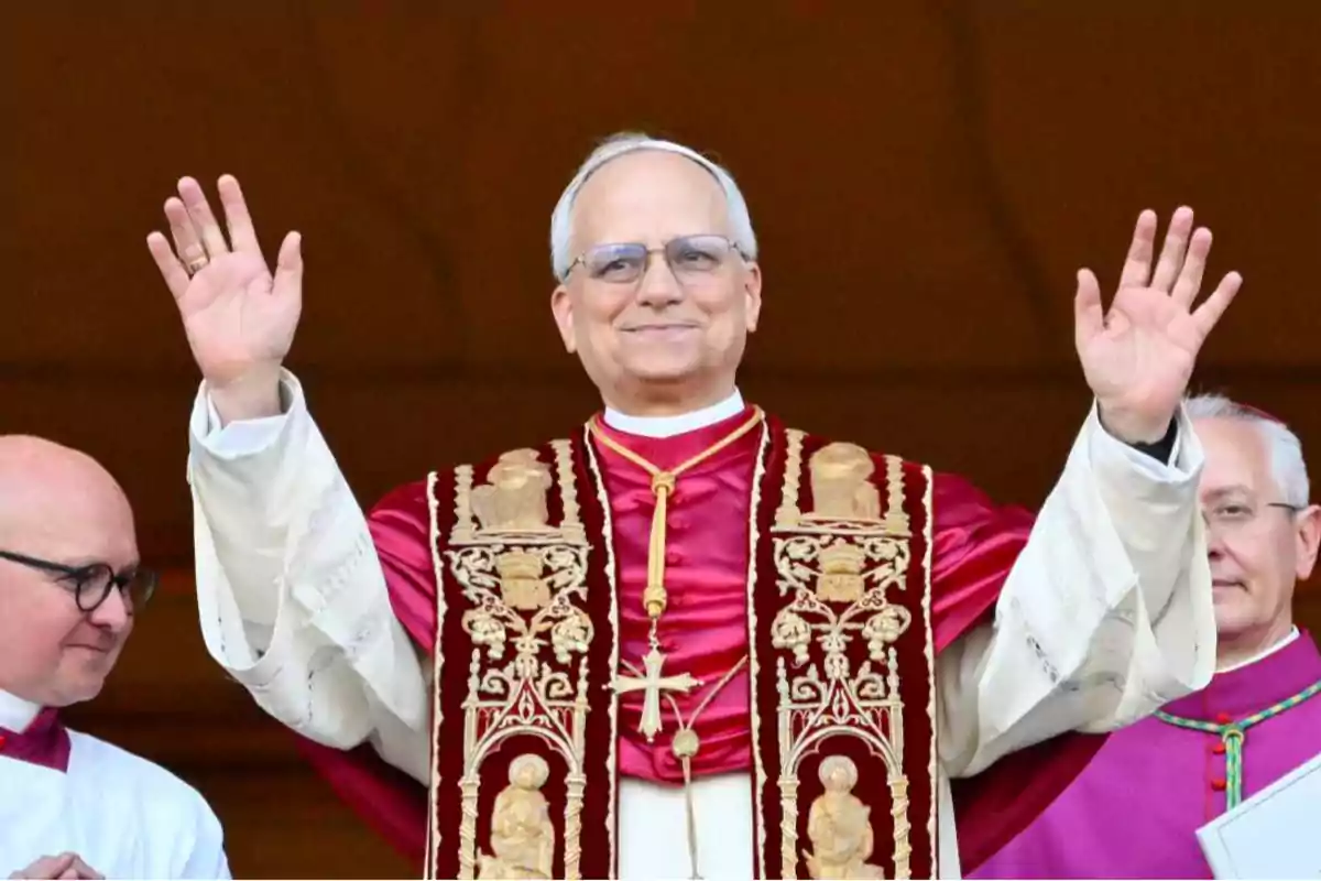 Un hombre con vestimenta religiosa levantando las manos y sonriendo, acompañado de otras personas. Un hombre con vestimenta religiosa levantando las manos y sonriendo, acompañado de otras personas.