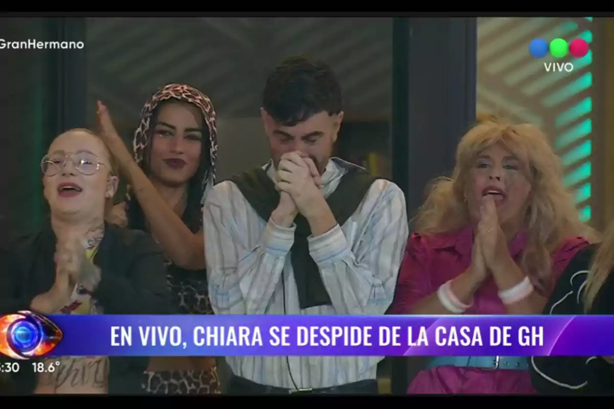 A group of people claps and shows emotions while a man in the center appears excited, with his hands together in front of his face, on a live television show. A group of people claps and shows emotions while a man in the center appears excited, with his hands together in front of his face, on a live television show.