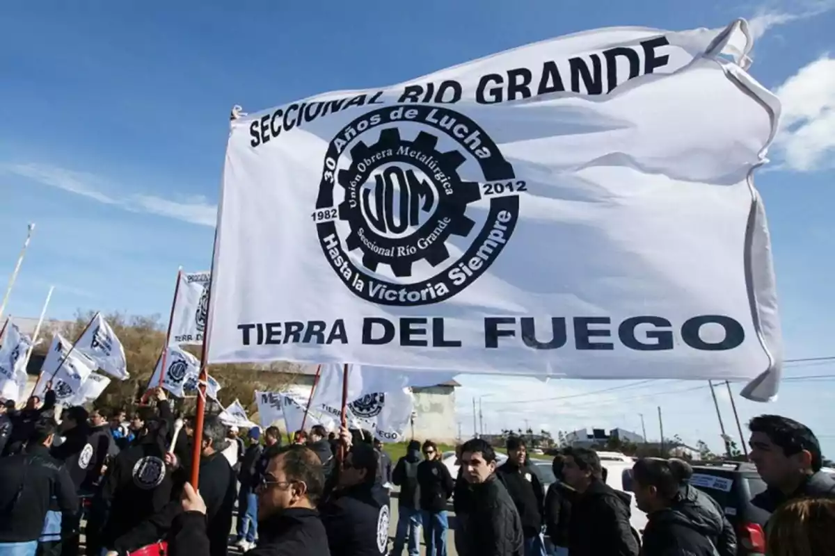 Un grupo de personas sostiene una bandera blanca con inscripciones de la Unión Obrera Metalúrgica en un evento al aire libre en Tierra del Fuego.