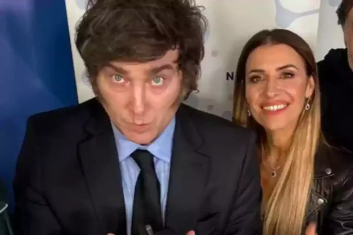 Un hombre de cabello castaño y una mujer de cabello largo y rubio posan juntos sonriendo frente a una pared clara Un hombre de cabello castaño y una mujer de cabello largo y rubio posan juntos sonriendo frente a una pared clara