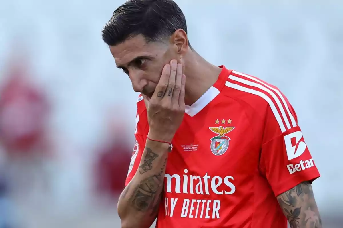 Futbolista con uniforme rojo del Benfica tocándose la cara con expresión pensativa en el campo de juego Futbolista con uniforme rojo del Benfica tocándose la cara con expresión pensativa en el campo de juego