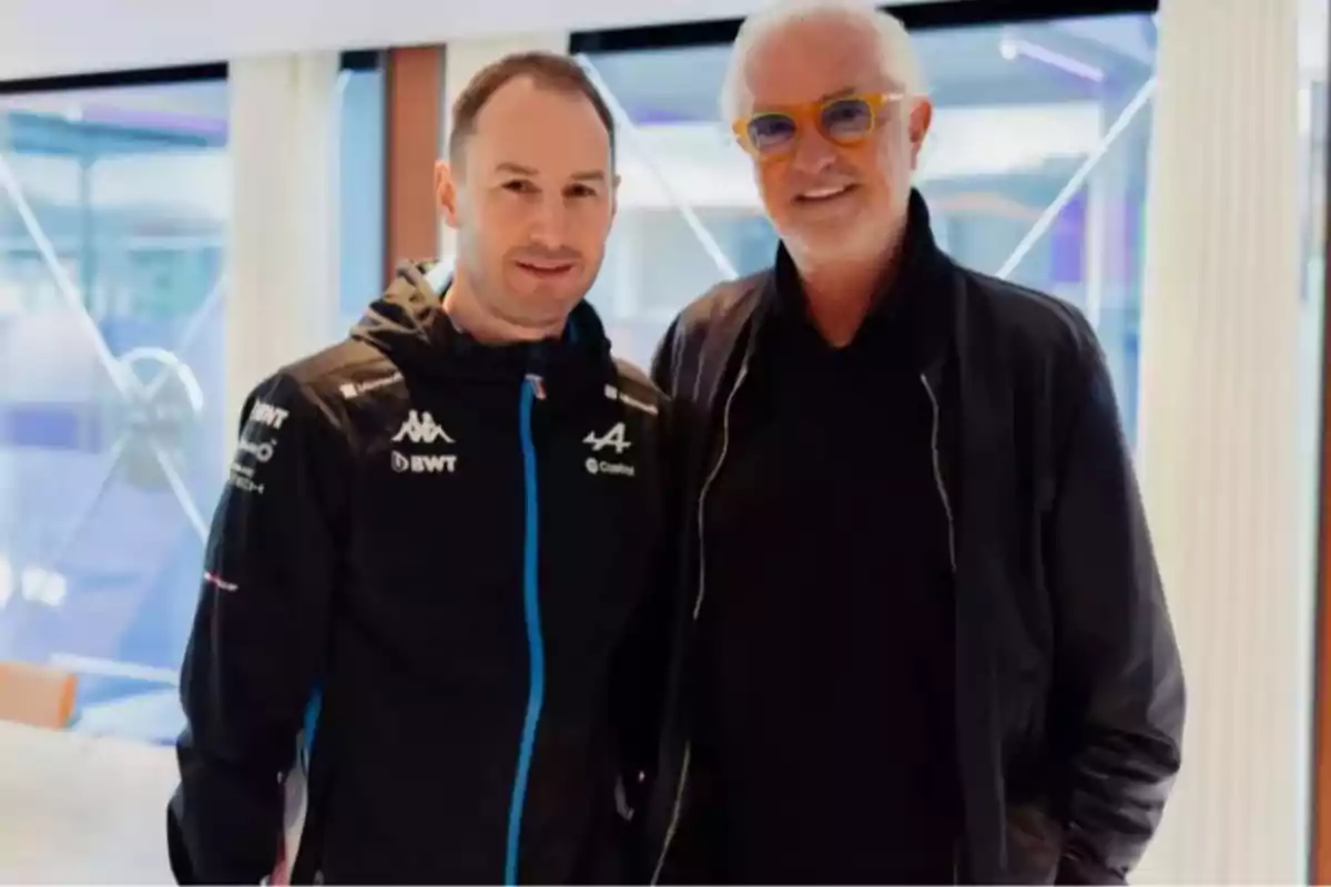 Two men pose together in a well-lit indoor setting, one wearing a sports jacket and the other wearing glasses and a dark jacket. Two men pose together in a well-lit indoor setting, one wearing a sports jacket and the other wearing glasses and a dark jacket.
