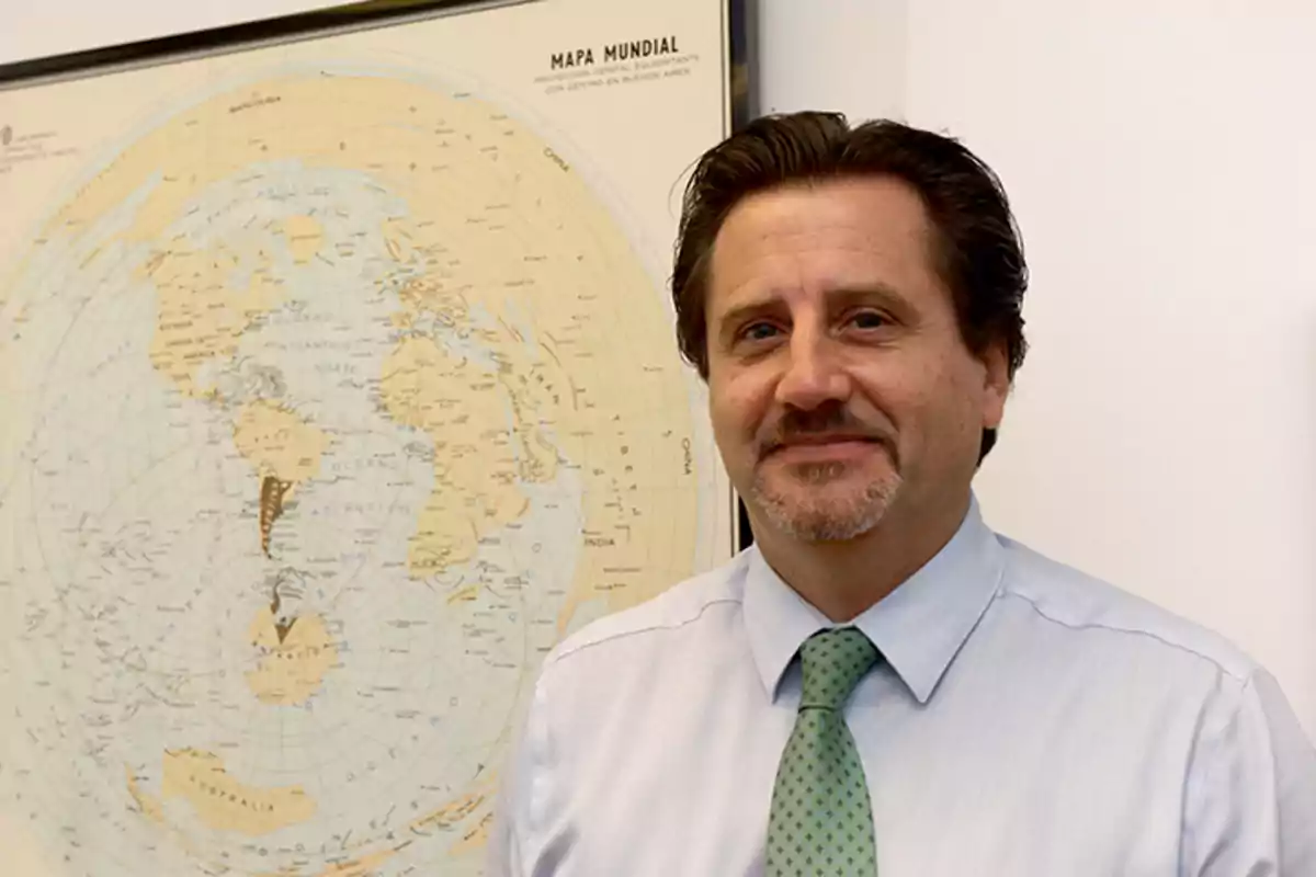 Middle-aged man wearing a light blue jersey and green tie posing in front of a world map on the wall Middle-aged man wearing a light blue jersey and green tie posing in front of a world map on the wall