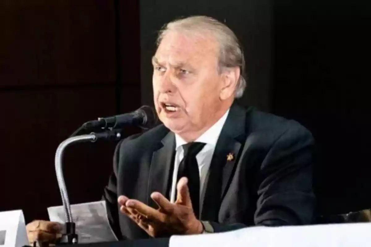 Elderly man with gray hair dressed in a dark suit speaking into a microphone during a formal event Elderly man with gray hair dressed in a dark suit speaking into a microphone during a formal event