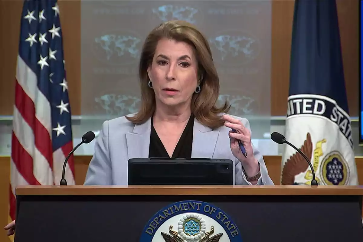 Mujer hablando en una conferencia de prensa en un podio del Departamento de Estado de Estados Unidos con banderas y un escudo oficiales al fondo Mujer hablando en una conferencia de prensa en un podio del Departamento de Estado de Estados Unidos con banderas y un escudo oficiales al fondo