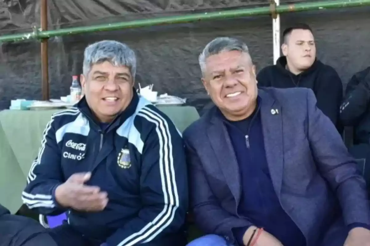 Dos hombres sentados juntos sonriendo en un entorno al aire libre.