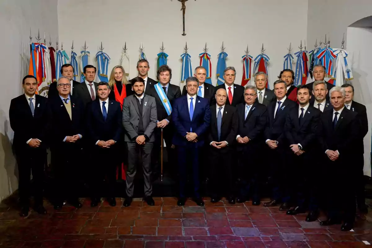 Un grupo de personas vestidas formalmente posando en una sala con banderas en el fondo.