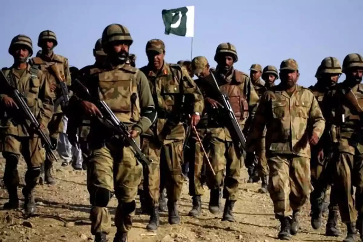 A group of soldiers in camouflage uniforms marches in formation with a flag waving in the background. A group of soldiers in camouflage uniforms marches in formation with a flag waving in the background.