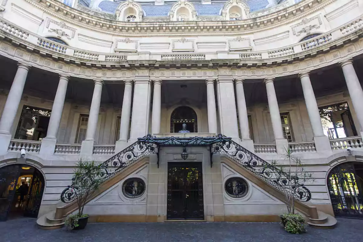 Fachada de un edificio histórico con columnas y una escalera central decorada con barandales ornamentales.