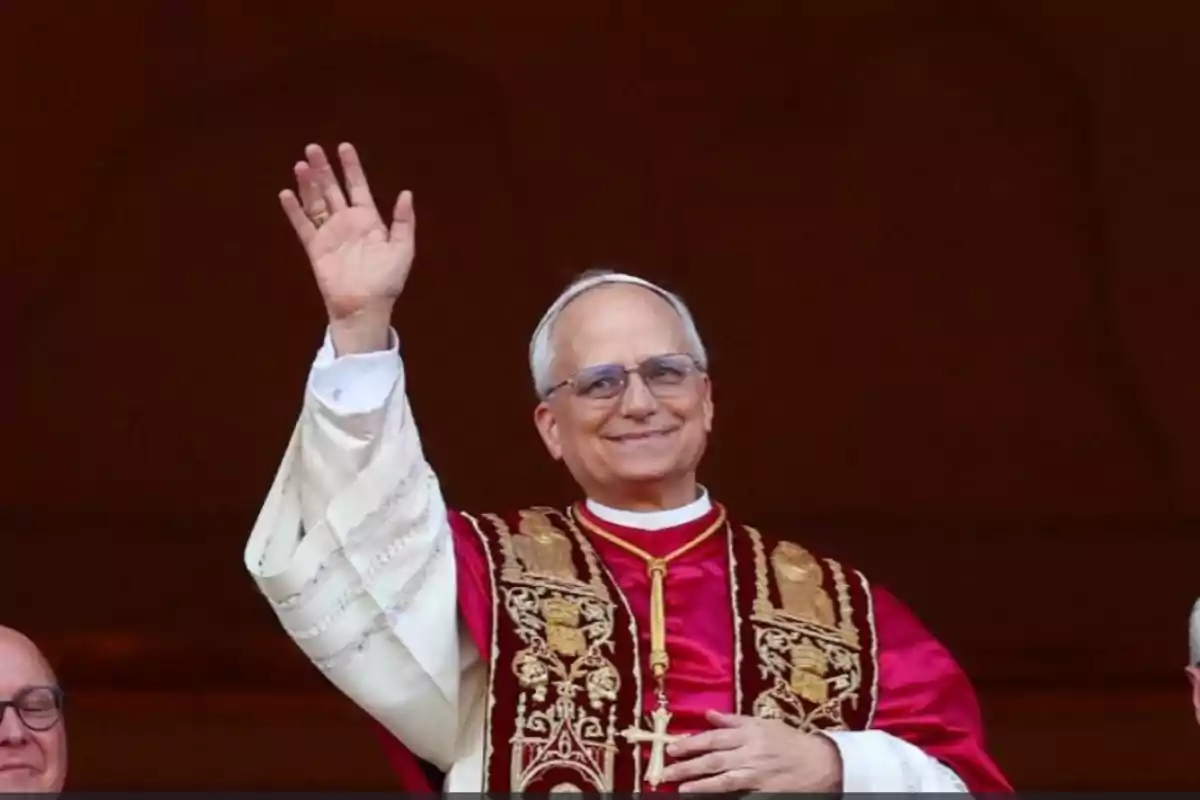 Hombre con vestimenta religiosa sonríe y saluda con la mano levantada