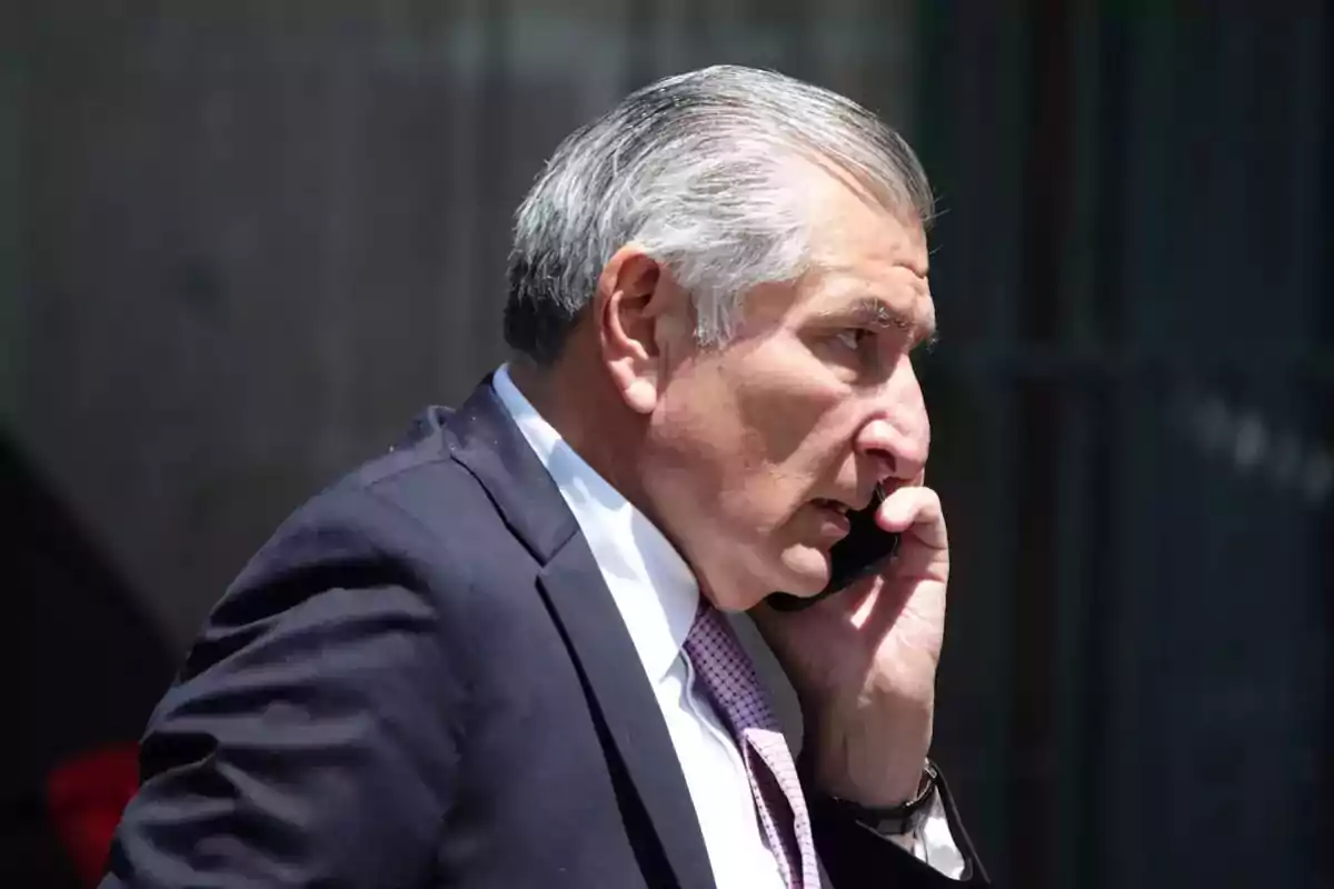 Hombre de cabello canoso hablando por teléfono móvil mientras viste traje oscuro y corbata. Hombre de cabello canoso hablando por teléfono móvil mientras viste traje oscuro y corbata.