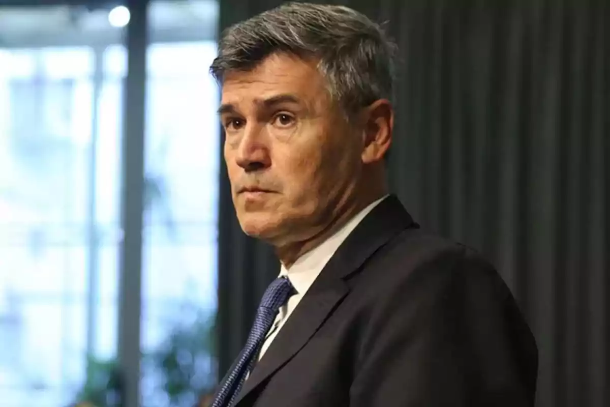 Gray-haired man in a dark suit and blue tie looking to the side in a professional indoor setting