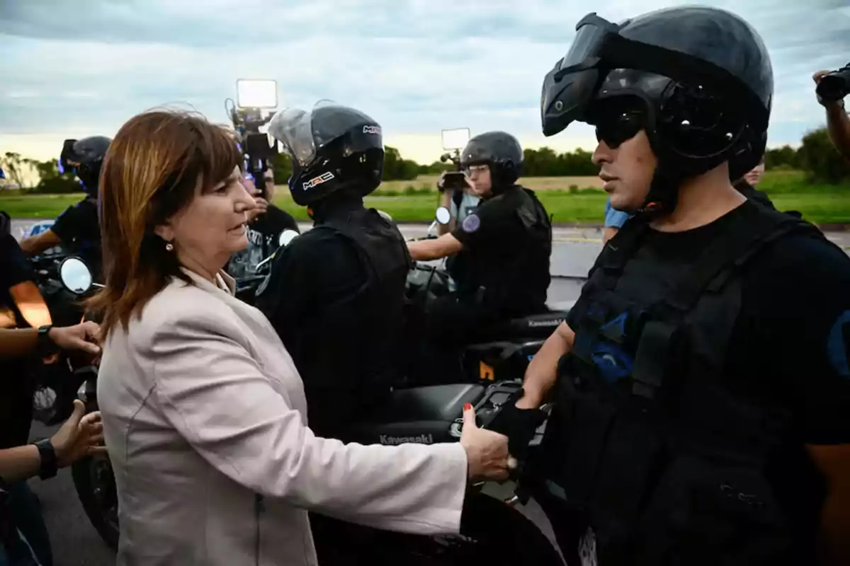 Una mujer estrecha la mano de un policía motorizado mientras otros oficiales están en el fondo.