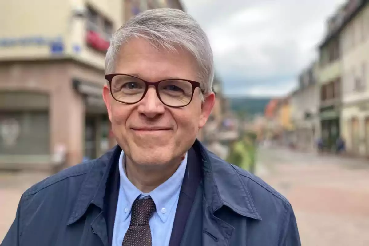Gray-haired man with glasses smiles while standing on a blurred urban street Gray-haired man with glasses smiles while standing on a blurred urban street