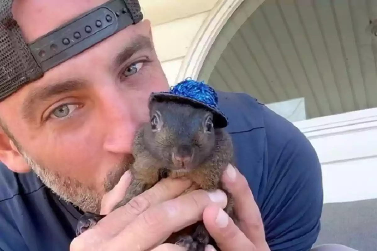 Un hombre con gorra sostiene a una ardilla que lleva un pequeño sombrero azul.