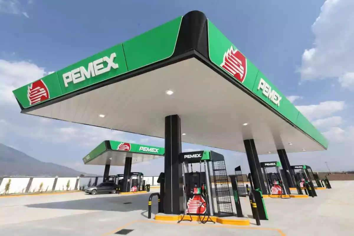 Una estación de servicio de PEMEX con techo verde y negro y varias bombas de gasolina en un día soleado.