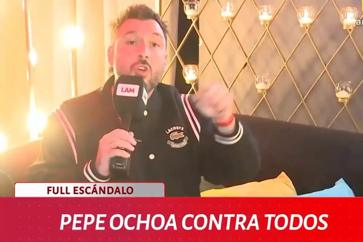 Un hombre con barba sostiene un micrófono de LAM mientras está sentado en un sofá con cojines de colores y luces decorativas en el fondo. Un hombre con barba sostiene un micrófono de LAM mientras está sentado en un sofá con cojines de colores y luces decorativas en el fondo.