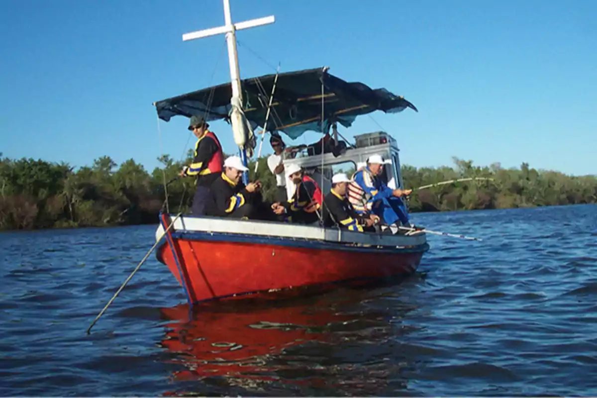 A group of people fishing in a red boat on a river on a sunny day