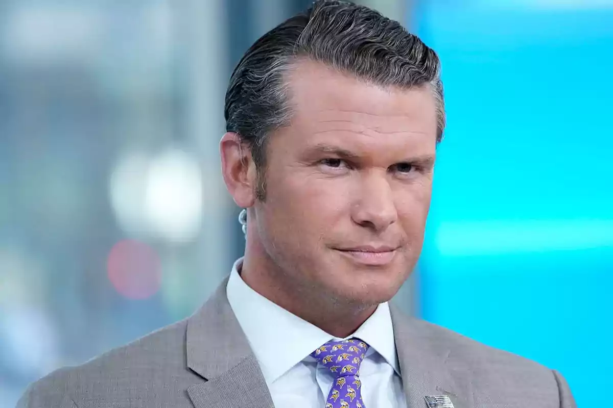 Short-haired man with slicked-back hair wearing a gray suit and a purple patterned tie, blurred blue and gray background. Short-haired man with slicked-back hair wearing a gray suit and a purple patterned tie, blurred blue and gray background.