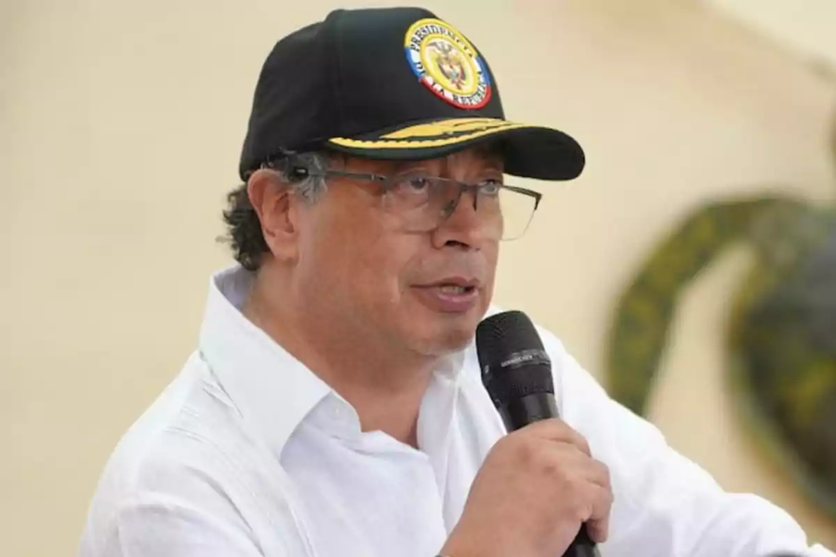 A man with glasses and a black cap speaks into a microphone while wearing a white jersey. A man with glasses and a black cap speaks into a microphone while wearing a white jersey.