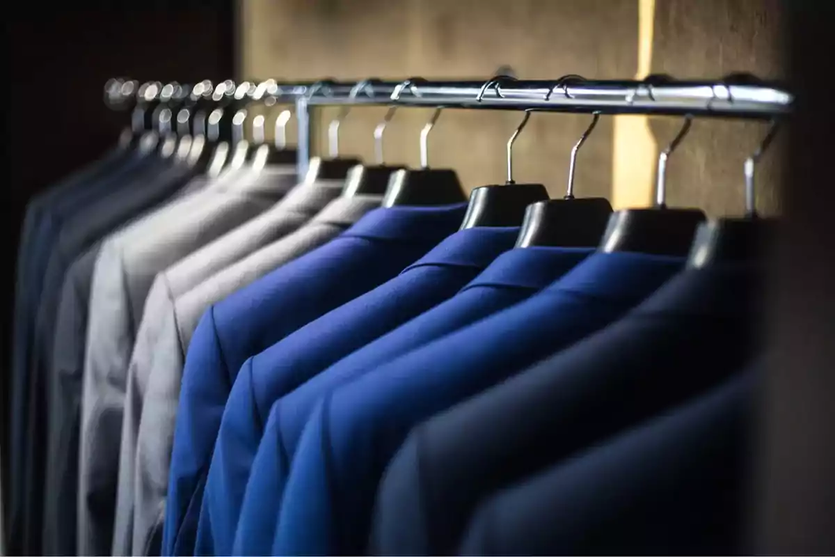 Suits hanging on a rod inside a closet.