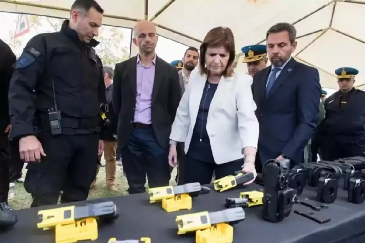 Un grupo de personas observa una mesa con dispositivos de seguridad en una exhibición al aire libre.