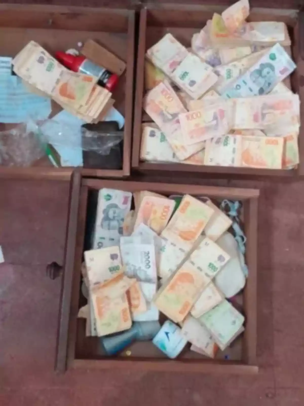 Three open wooden drawers filled with Argentine bills of different denominations and some small objects