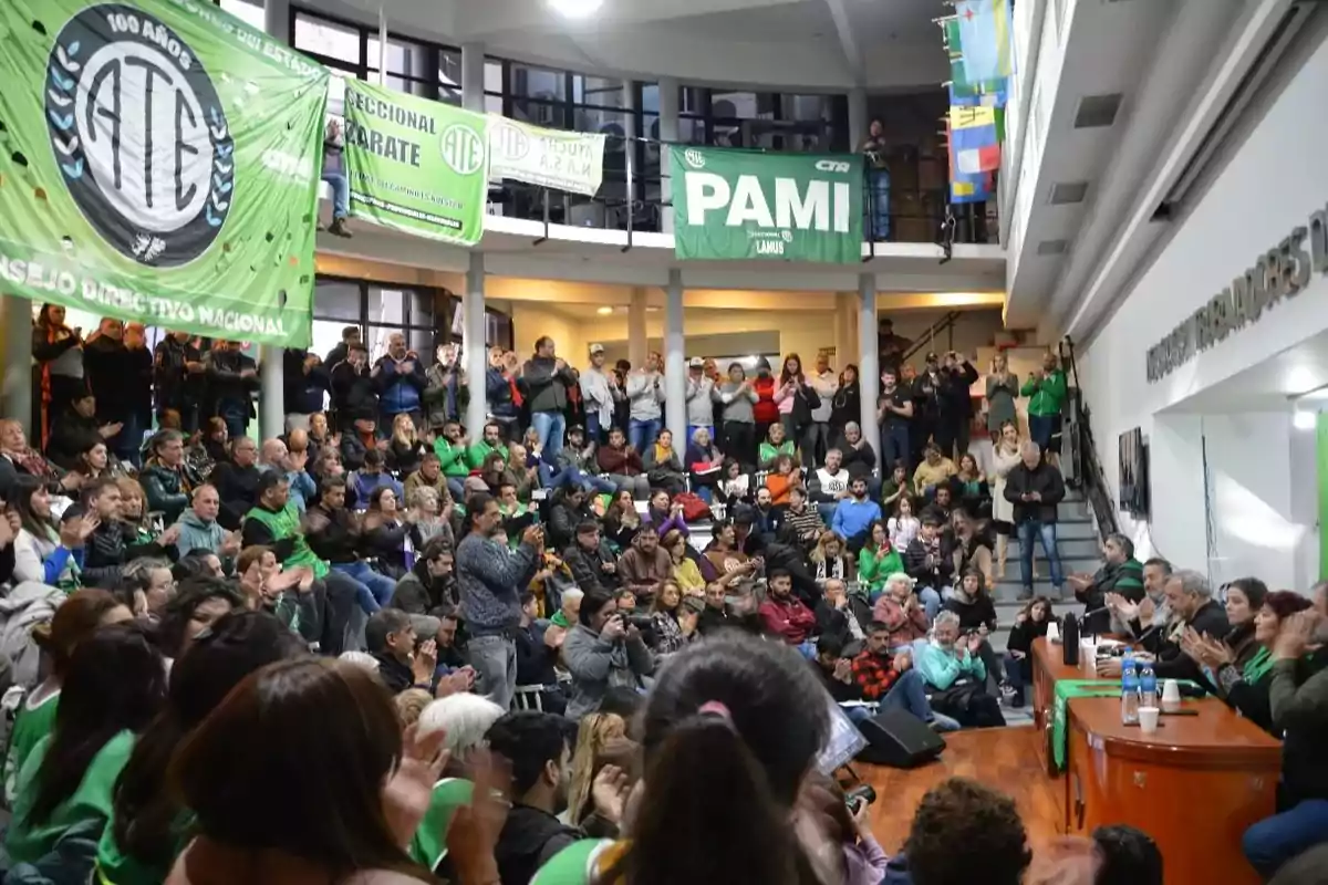 Una multitud de personas se reúne en un auditorio con banderas verdes colgadas en el balcón superior.